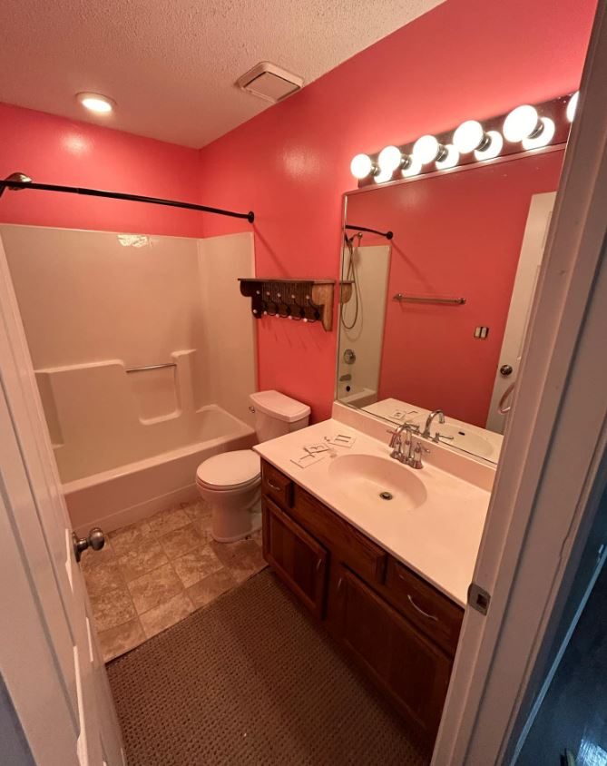 Bathroom before remodeling with a fiberglass tub-shower combination, coral walls and a wood vanity